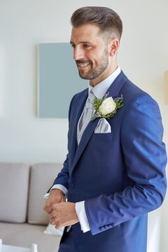 Smiling fiance in classy suit standing in bright living room of modern apartment during wedding fees