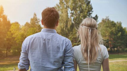 Young man and woman stand with their backs in the park