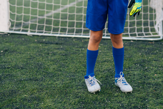 Crop girl in white and blue uniform with soccer ball while standing alone on green field in modern sports club