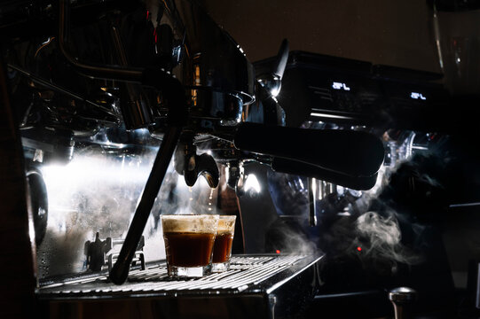 Glasses with hot coffee placed on metal panel of professional coffee maker in dark cafe