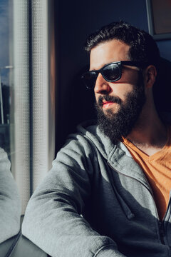 Thoughtful young bearded man looking through window while traveling by train
