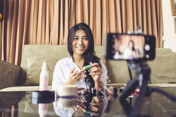Asian businesswoman working from home live video interaction with customers using camera device vlogging selling make up products, viral internet social media influencer interacting to live audience