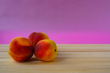 Three ripe peaches on a wooden table and pink background