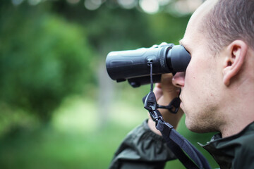 A young hunter in the forest looks into the binoculars. He is trying to find some wild animals.