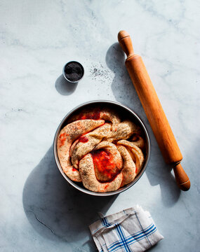 From above fresh strawberry brioche on the making placed near rolling pin and kitchen utensils on white modern marble table