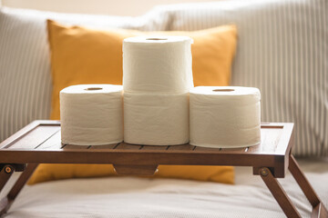 Toilet paper stacked on top of a wooden table inside of a bedroom. Toilet paper is a hot commodity during the Coronavirus pandemic. Sold out in all stores as people panic buy - 364559854