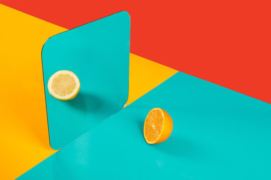 Vibrant background with mirror reflection of half of fresh orange as lemon on blue surface in composition with empty red and yellow areas like concept of perception in three dimensional space and distortion of imagination
