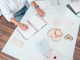 Unrecognizable lady in elegant outfit sitting at office desk and writing in open notebook