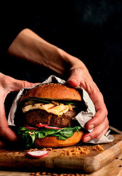 Cropped unrecognizable person holding delicious vegan lentils hamburgers placed on wooden board on dark background
