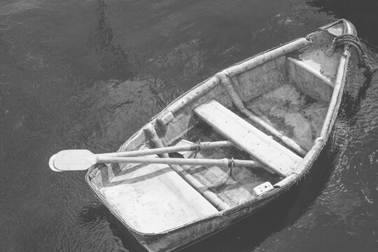 Black and white from above of small fishing boat with oars on water surface in bay