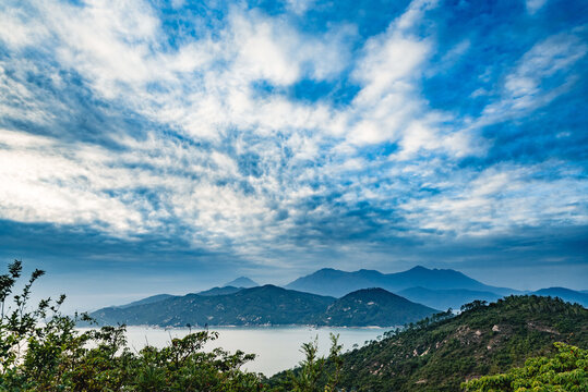 Picturesque view of green shore with bay and misty mountains under blue sky with clouds