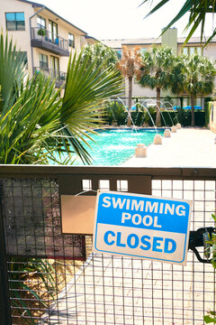 Closed sign with warning inscription placed on grid gate near swimming pool