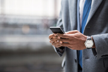 Faceless shot of black businessman in suit and watch using smartphone outside.