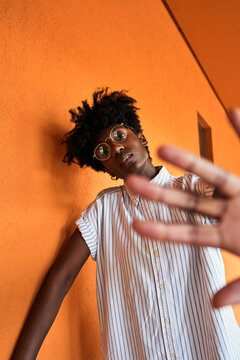 Adult African American female with eyes closed trying to stop negative impact while standing with arms raised against blurred vivid orange interior in corridor of modern building