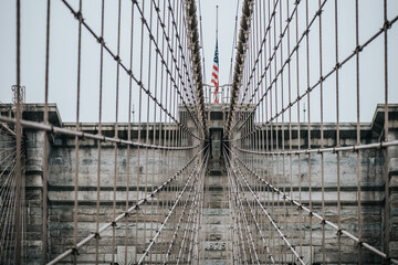 Low angle of stone towers with pointed arches of suspension Brooklyn bridge with American flag on cloudy day