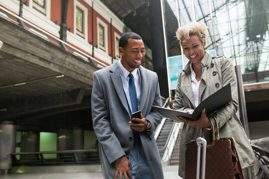 Cheerful laughing black man and woman in trendy elegant clothes having fun while standing with papers on stairs.