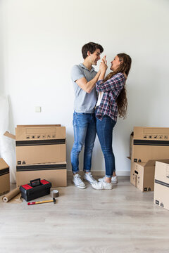Young couple laughing and playing around in room with carton boxes and repair instruments on floor