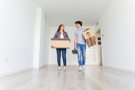 Young couple walking in empty room carrying carton boxes and tool bag