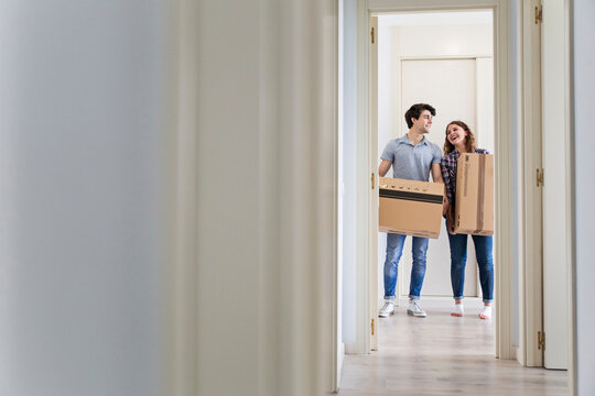Young couple moving carton boxes in new empty apartment with opened door