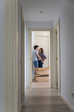 Young couple moving carton boxes in new empty apartment with opened door