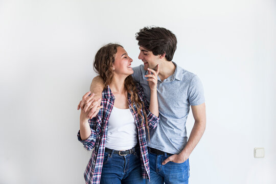 Young couple in casual wear kissing and holding hands standing in room with white empty wall