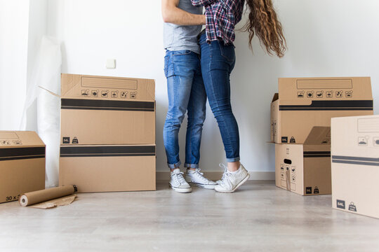 Crop view of couple in casual clothes hugging standing in room with carton boxes