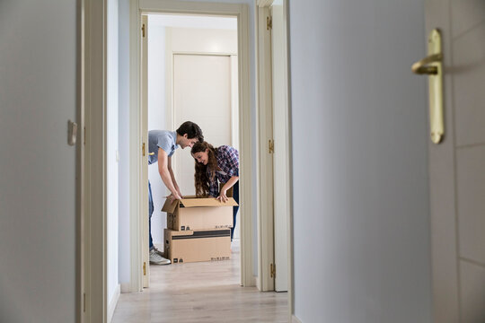 Young couple moving carton boxes in new empty apartment with opened door