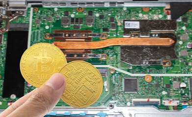 Bitcoin holding in hand with motherboard blurred background.