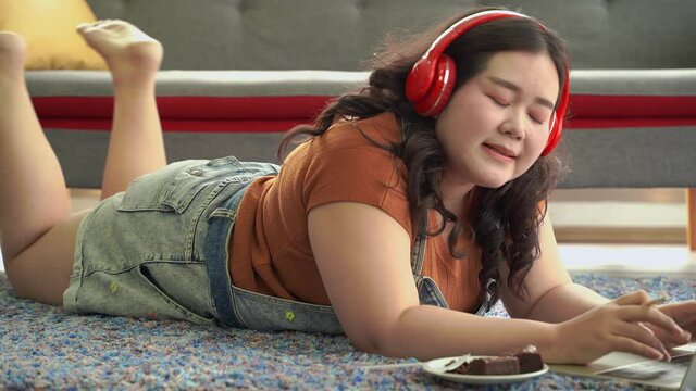 pan video shot,An Asian fat woman is lying down on the floor and working at home. At the same time, she ate food, being an unhygienic lifestyle.
