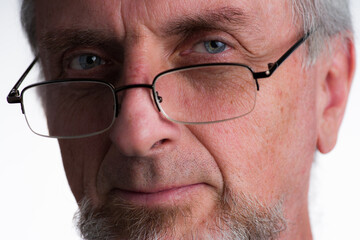 Mature man in 40s 50s or 60s with gray grey hair and beard or goatee looking over rim of eye-glasses with amused look in eyes, tight crop close-up portrait.