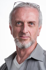 Mature man with gray grey hair and beard or goatee eye blues, unbuttoned gray shirt looking at camera, eye-glasses on head, confident, amused look in eyes, close-up portrait  white background