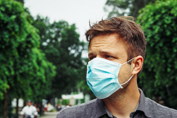 Handsome young European man in a park with a medical face mask on. Closeup of a 35-year-old male in...