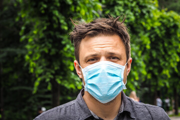 Handsome young European man in a park with a medical face mask on. Closeup of a 35-year-old male in...