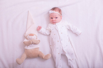 Portrait of a child on a white background with plush bear toy. Baby girl 1 months among toys. Space for text.