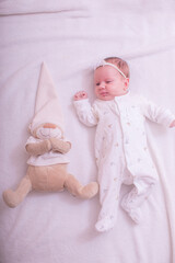 Portrait of a child on a white background with plush bear toy. Baby girl 1 months among toys. Space for text.