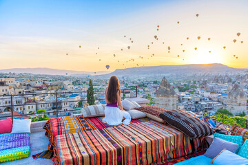 A woman sits on one of the Cappadocia roof in early morning sunrise, when balloons fly. Romantic scene Cappadocia, Turkey.