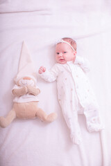 Cute baby girl on a light background in bed at home with teddy. Close up portrait of infant baby 1 months old. Image in pink rose gold color.
