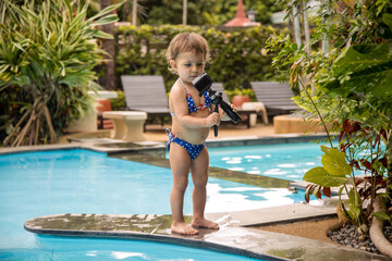 kid blogger school concept. cute baby holds action camera in swiming pool.