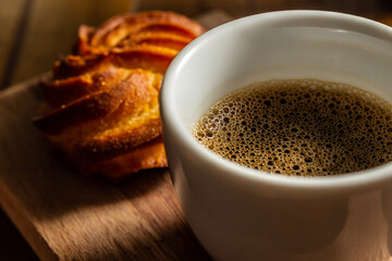 Close em café cem xícara branca e broa de milho ao fundo.