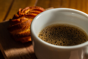 Close em café com espuma em xícara branca e broa de milho.