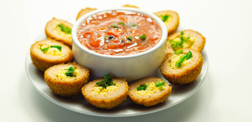 Mini scotch eggs with tomato sauce served on the white ceramic plate