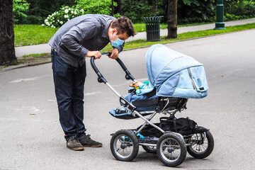 Handsome young European man on the street with a medical face mask on and baby carriage....