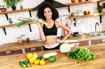 A sportive african-american girl going to prepare salad in a kitchen at home, she holds leek and...