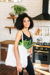 Healthy lifestyle concept. Young sporty african-american woman in the kitchen with a shopping bag full of fresh vegetables