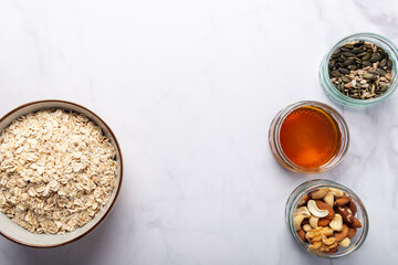 Ingredients for healthy homemade granola with Gluten Free Rolled oats or porridge oats, variety of chopped nuts and seeds, and maple syrup. Preparation for cooking at home. Marble background