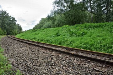 Obraz premium Old railroad tracks against the backdrop of a grassy flood embankment.