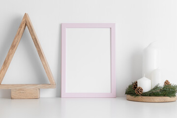 Pink frame mockup with a wooden tree and candles on a white table. Christmas decoration.
