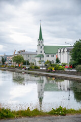 Fototapeta na wymiar REYKJAVIK, ICELAND - AUGUST 11, 2019: Lake Tjornin with church on a cloudy summer day