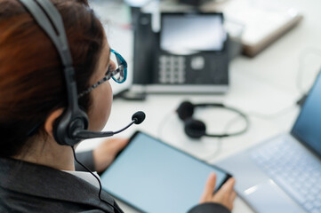 Rear view of a woman in a headset using a digital tablet while sitting at a desk. Friendly female support service operator at work.