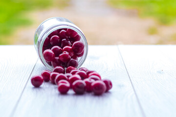 Fresh collected red cherry in a glass jar. Berries are scattered on a wooden background